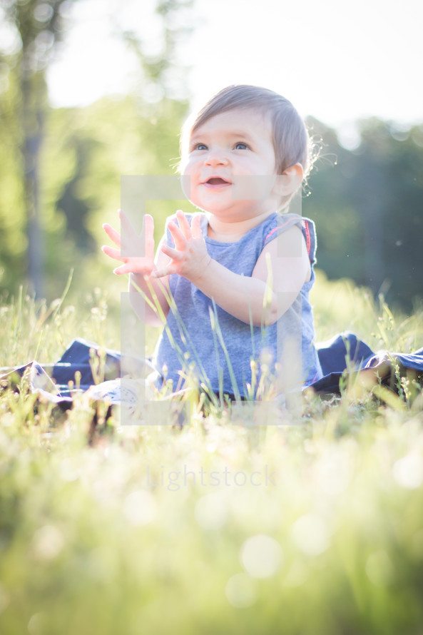 toddler girl sitting in grass clapping her hands 