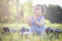 a toddler girl sitting in grass clapping her hands 