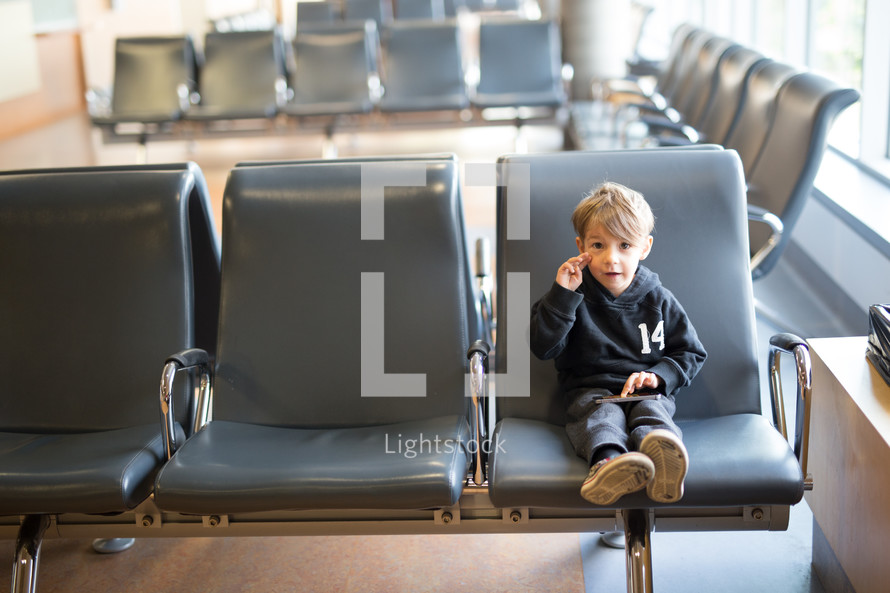 a boy child in a waiting area playing on a cellphone 