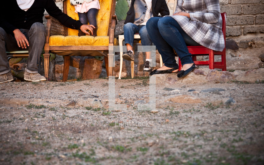 Family sitting in chairs in the dirt outside.