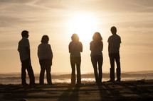 Sun shining on five young people standing on the beach.
