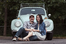 a couple sitting in front of a vintage Volkswagen Beetle 