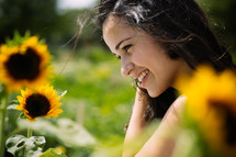 A smiling young woman standing among sunflowers.