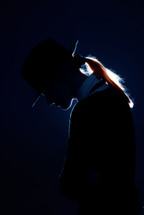 Sad woman in hat on a dark background with back-lighting