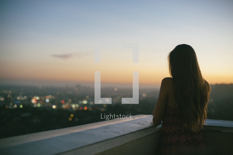 woman looking over a balcony at distant city lights 