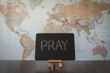 world map and word pray on a sign 