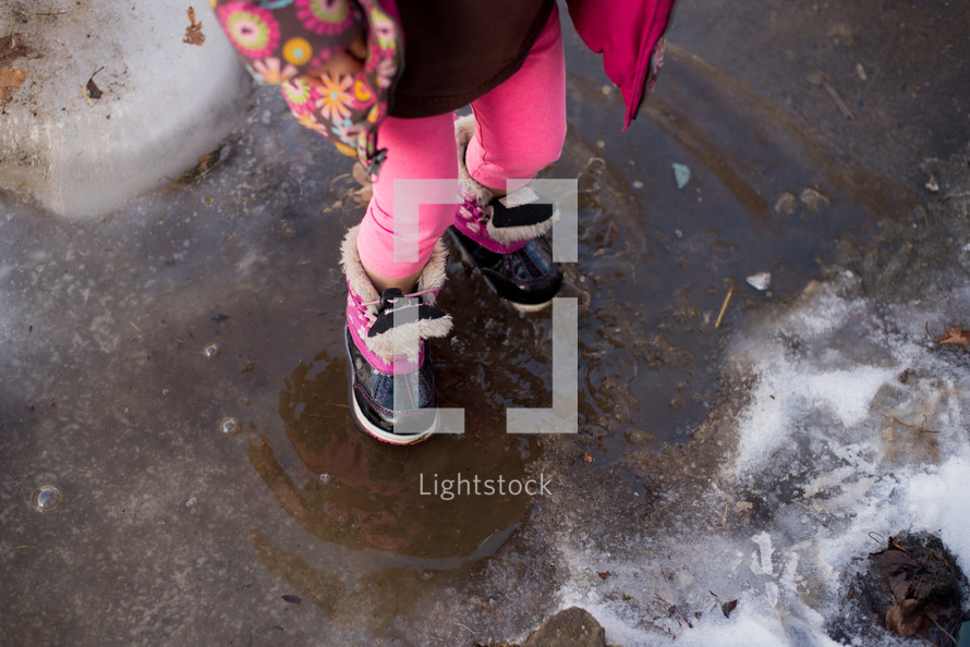 a girl splashing in melting snow on a sidewalk 