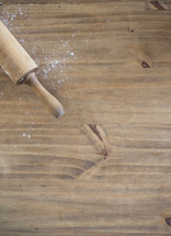 A rolling pin on a cutting board with a dusting of flour.