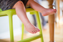 A toddler's legs hanging from a high chair.