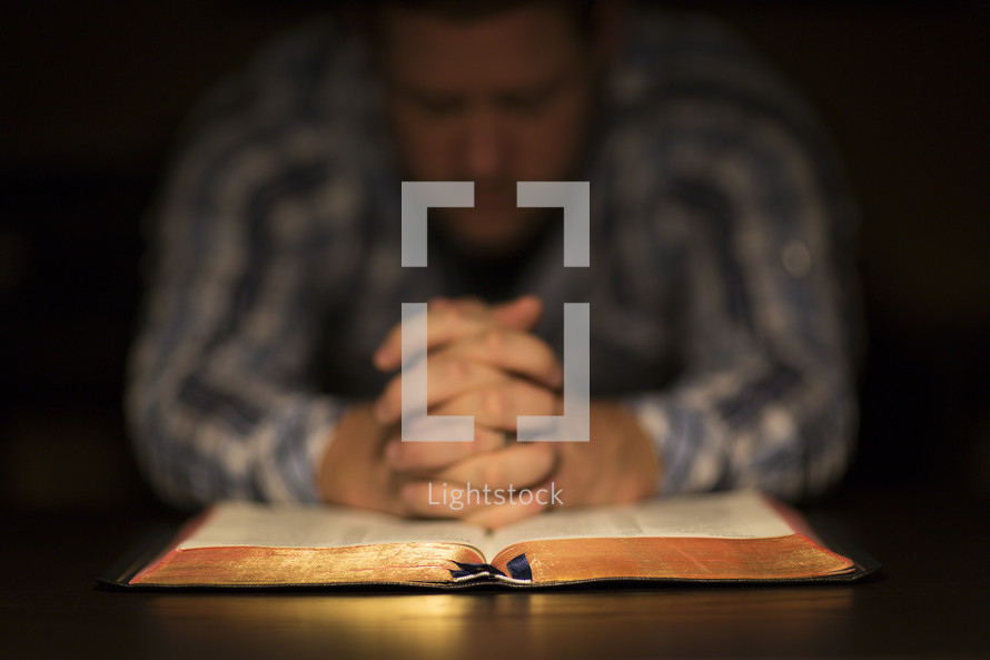 A man praying over an open Bible.