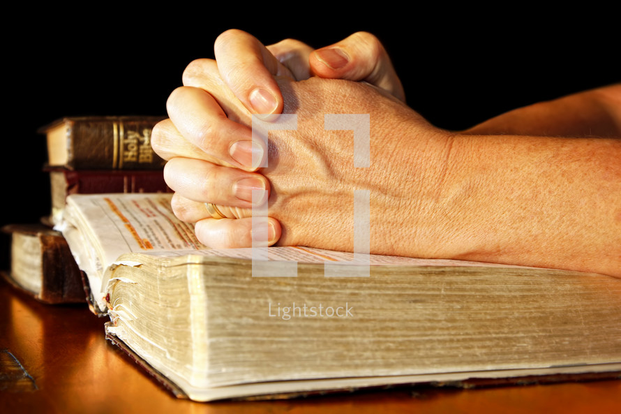 Praying Hands in Light with Holy Bibles  -  A man folds his hands in committed prayer over a Holy Bible, while light shines directly on his hands and the open bible.