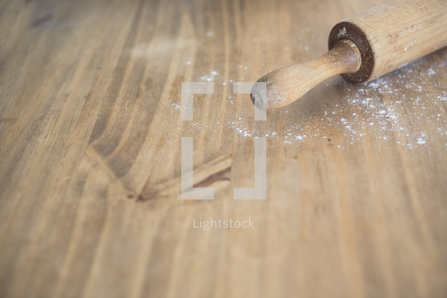 A rolling pin on a cutting board with a dusting of flour.
