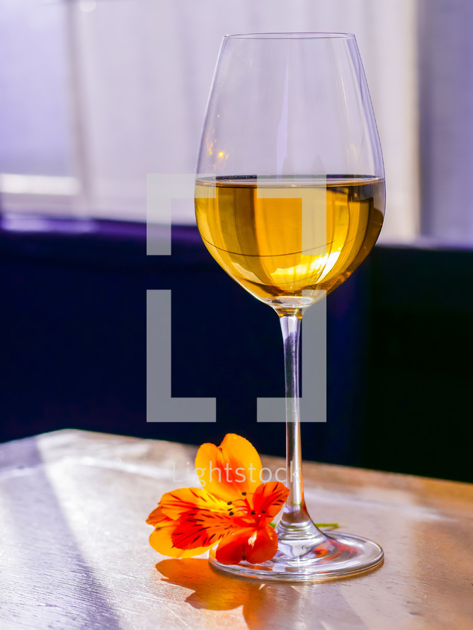 Glass of white fine wine with flower on vintage shabby wooden table in restaurant.