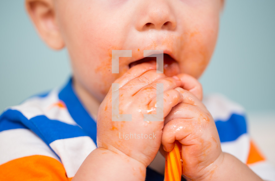 a toddler boy with a sticky messy face eating a lollipop 