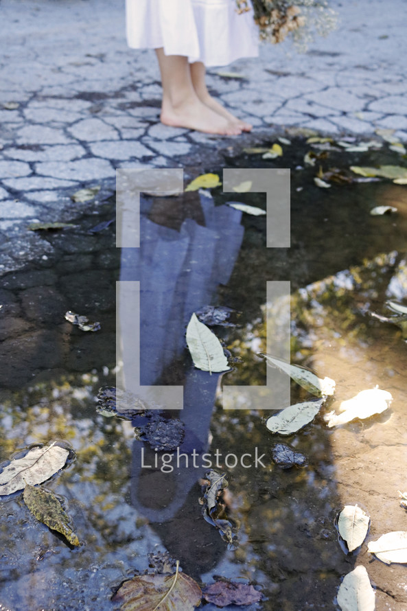 barefoot girl in a white dress standing by a puddle 