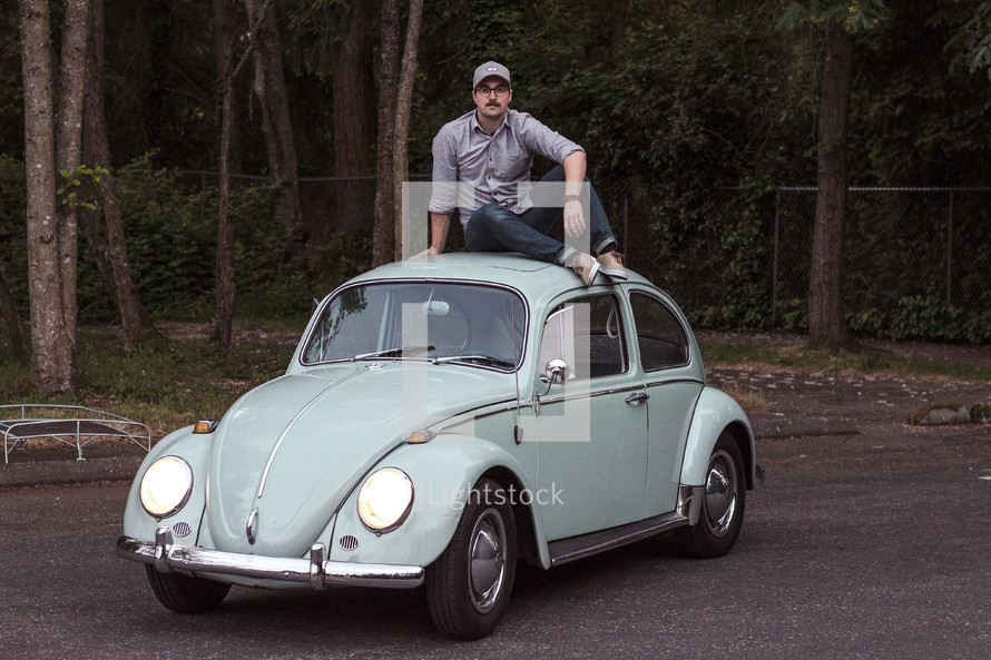 a man sitting on a vintage Volkswagen Beetle 