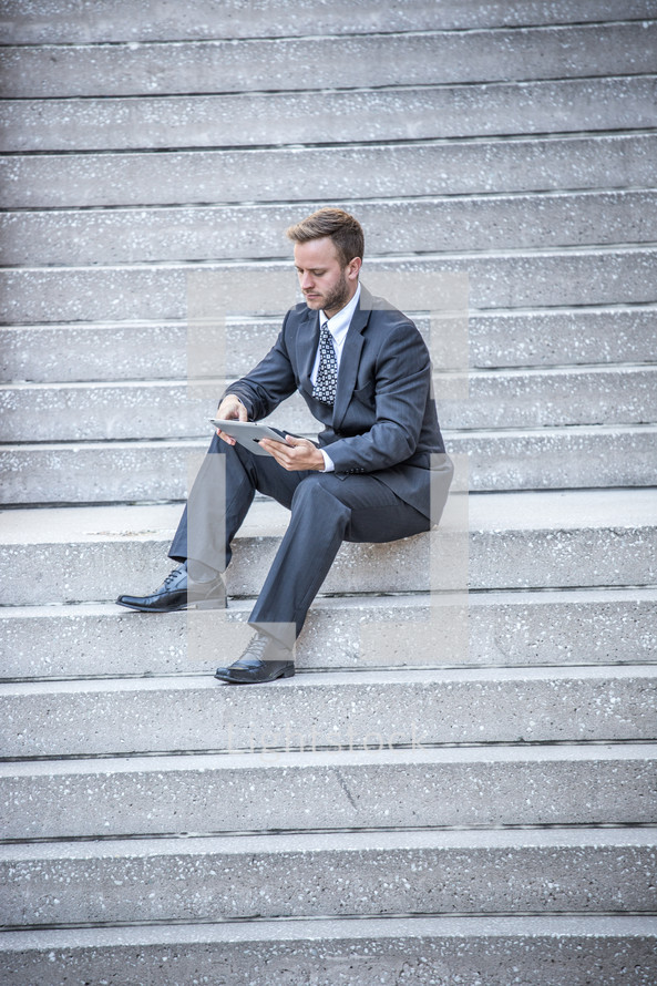 a businessman sitting on steps holding a tablet 