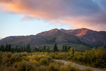 Colorful clouds over alaskan mountain range landscape near trees and brush