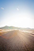 paved road under bright sunlight through a desert 