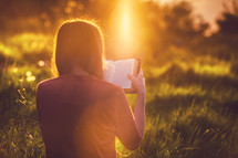 Girl reading the Bible at sunset