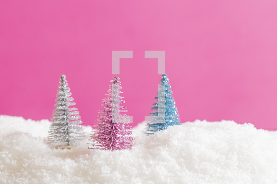 Pink, silver, and turquoise Christmas trees in powdery snow on pink background