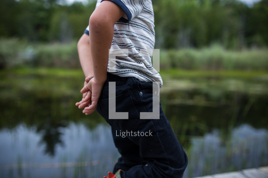 a boy standing in front of a pond 