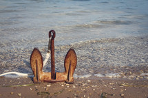 rusty anchor sitting upright on a shore