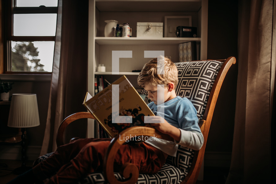 a little boy sitting in a chair reading a book 