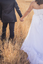 bride and groom walking through a field 