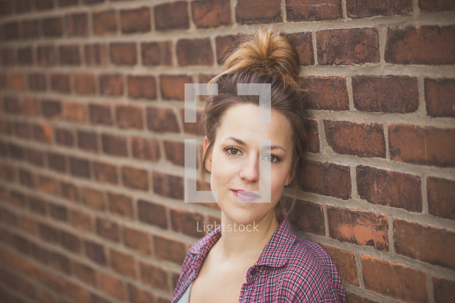 A young woman leaning against a brick wall.