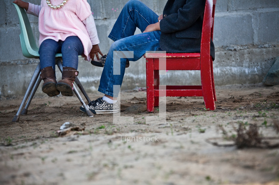 Children sitting in chairs in the dirt.