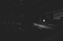 Man speaking on stage in filled auditorium.