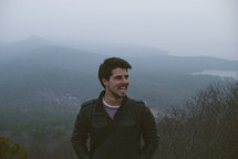 man standing outdoors in front of a foggy mountain 