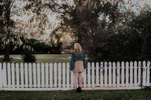 a young woman standing in front of a white picket fence 