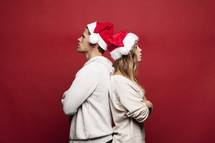 man and woman in santa hats back to back not speaking to each other