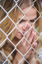 a woman clinging to a chain link fence with praying hands 