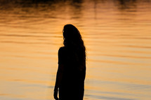 silhouette of a woman standing in front of water at sunset 