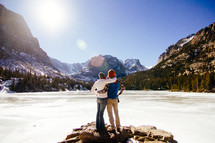 a couple hugging in front of a frozen lake 