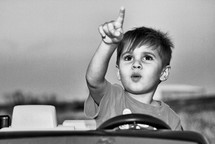 Boy in a toy car pointing at the sky