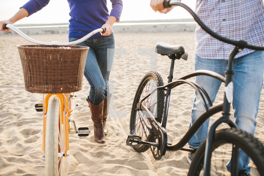 man and woman pushing beach cruiser bicycles on the beach