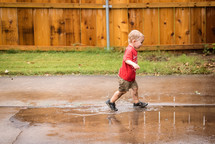 a toddler boy splashing in a puddle 