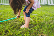 little girl playing with a water hose in grass 
