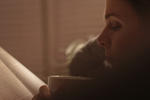 a woman reading a book and drinking hot tea 