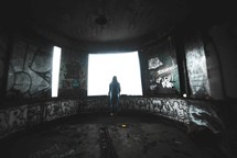 a person standing in a graffiti covered room looking out a window 