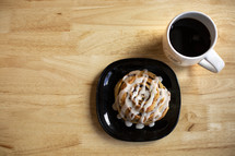 cinnamon bun and coffee mug on a wood table 