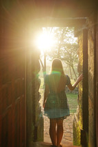 a woman standing in sunlight at the entrance of a door 