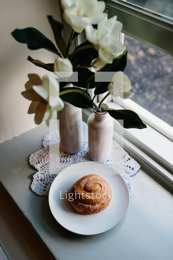cinnamon bun on a plate on a table by a window 