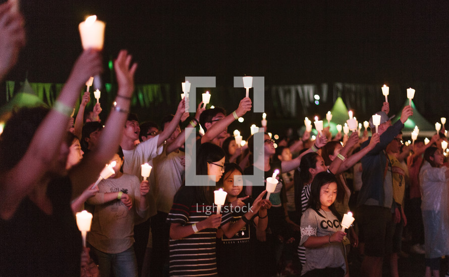 a crowd holding up candles at a worship service 