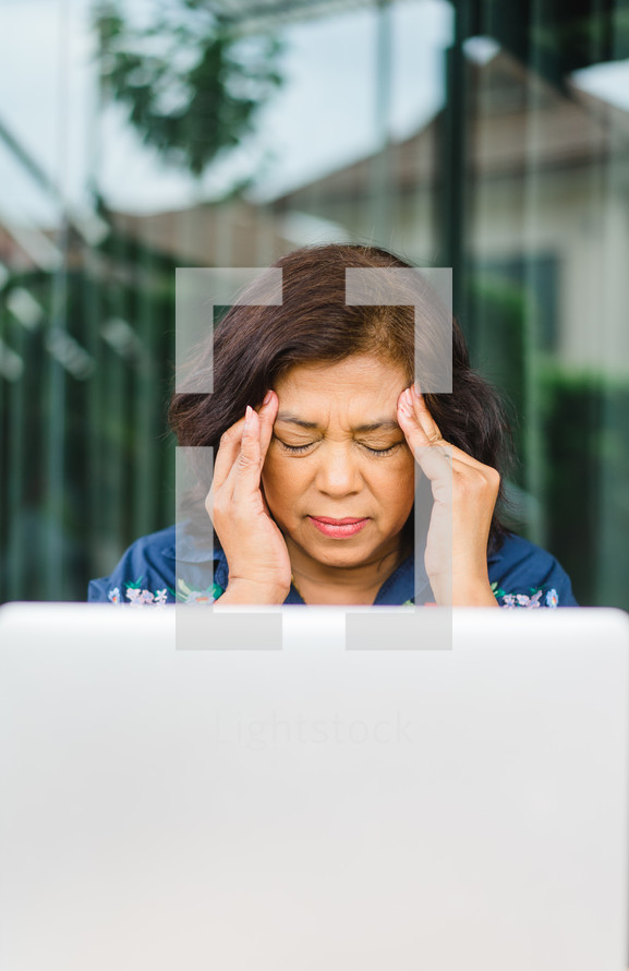 woman sitting behind a computer with a headache 