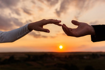 Hands of bride and groom reaching each other, touching fingers on sunset sky countryside background. Helping hands for save and support people concept. Wedding day. Valentine day